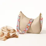 Blue and coral patterned strap attached to a beige shoulder bag beside a folded scarf