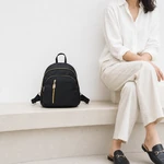 Black mini backpack on a pale ledge beside a seated person wearing light-colored clothing