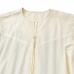 Close view of the light-yellow robe’s round-neck finish, short front opening and tassel and sleeve seam.
