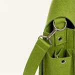 Gros plan sur le sac vert montrant le clip métallique de la bandoulière, l'anneau latéral, les œillets et la poche en feutre
