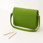 Sac à bandoulière vert en feutre à côté de deux crayons, avec sa bandoulière assortie bouclée devant