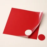 Red puff HTV sheet with a circular cutout and the matching round piece beside it, illustrating cutting.