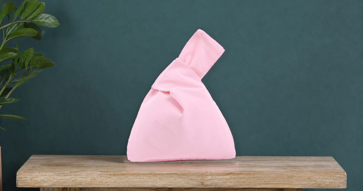 Bolsa japonesa de nó em algodão rosa sobre um banco de madeira na entrada