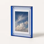 Blue-edged acrylic frame with a cloud photo on a pale tabletop
