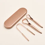 Tres raspadores linguales en oro rosa con un estuche cerrado a juego sobre un fondo marfil cálido.