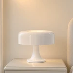 White mushroom table lamp with a rounded shade and pedestal base on a bedside table, softly lit.