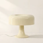 Beige-yellow mushroom table lamp with rounded shade and pedestal base against white.