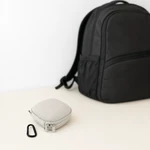 Hellgraue Filtertasche und schwarzer Clip auf einer Tischplatte vor einem schwarzen Rucksack