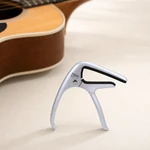Silver capo standing on a tabletop beside the body of an acoustic guitar