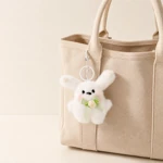White rabbit charm hanging from a beige tote handle; bag is a styling prop