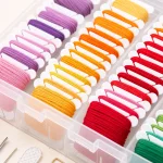 Nahaufnahme weißer Spulen mit violettem, rosa, gelbem, orangefarbenem und rotem Garn in durchsichtigen Fächern