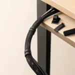 Close-up of a braided cable sleeve and clips guiding cords around a desk corner