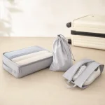Cubo grigio, borsa con coulisse e borsa per scarpe aperta disposti accanto a una valigia