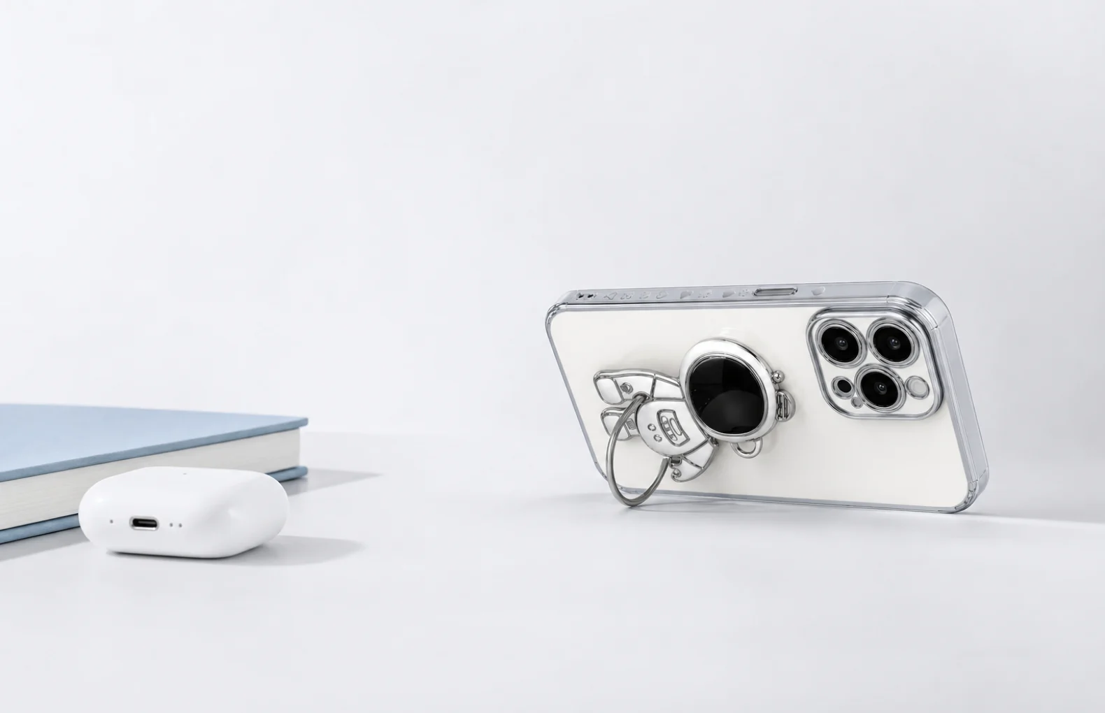 coque iPhone astronaute antichoc avec bord chrome et support depliable sur bureau clair