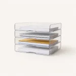 Vue en biais basse de quatre bannettes transparentes contenant papiers, carnet à spirale et dossier jaune