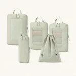 Pale green packing cubes with loop handles arranged beside a slim pouch and drawstring bag