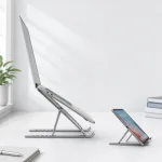 Vista laterale di un laptop su un supporto argentato inclinato, accanto a un telefono su un supporto separato più piccolo