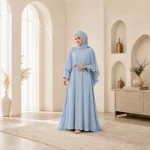 Femme portant une abaya bleu clair et un foulard assorti près de fenêtres cintrées