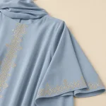Gros plan sur la bordure géométrique dorée du devant et de la large manche d'une abaya bleu clair