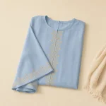 Abaya bleu clair pliée montrant une décoration dorée sur le devant et les manches, à côté d'un foulard