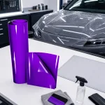 Purple gloss film roll and sample shown on a workbench beside a car and application tools