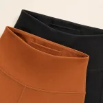 Primo piano delle alte cinture dei leggings marroni e neri, con aperture interne delle tasche e cuciture