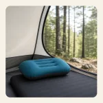 Blue inflated pillow on a dark sleeping mat inside a tent facing a wooded campsite