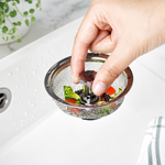 Hand holding the centre knob of a raised sink basket containing food scraps