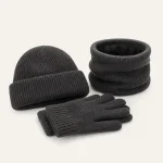 Schrägansicht einer dunkelgrauen Strickmütze, gestapelter Handschuhe und eines aufrecht stehenden Schlauchschals