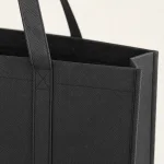 Gros plan sur le sac cabas noir, sa surface texturée, son anse cousue et son bord supérieur ouvert