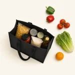 Vue du dessus d’un sac cabas noir rempli de provisions près de poivrons, tomates et laitue