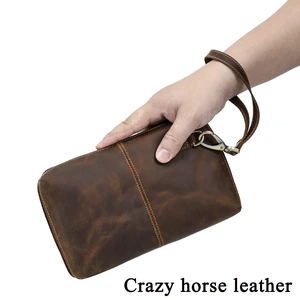 Hand holding the coffee leather clutch with its strap around the wrist and a Crazy horse leather label.