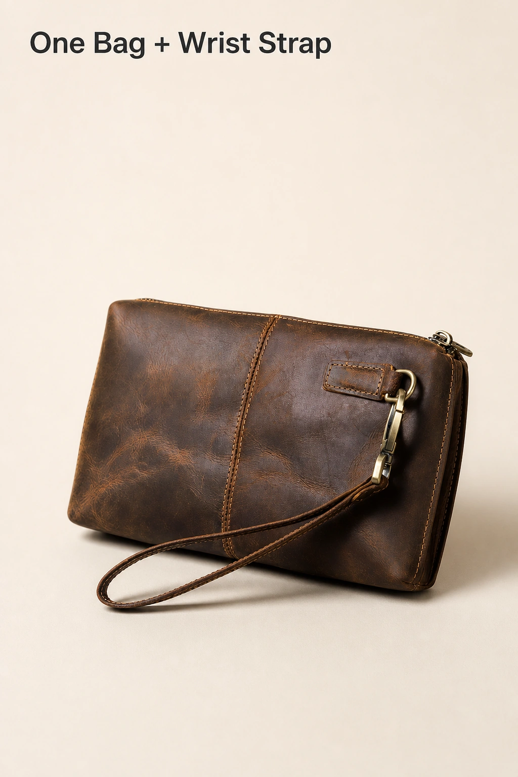 One coffee leather clutch with its clipped wrist strap and the heading One Bag + Wrist Strap on beige.