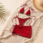 Bikini rosso con bordo leopardato e gonnellina corta disposto su tessuto accanto a un cappello di paglia