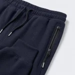 Gros plan sur un jogger bleu marine avec taille à cordon, poche zippée et bas de jambe côtelé