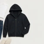 Felpa nera con cerniera stesa accanto a maglietta bianca, jeans blu e sneakers chiare
