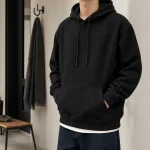 Hombre con sudadera negra con capucha sobre un top blanco y vaqueros oscuros en interior