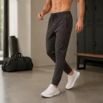 Man wearing dark gray joggers and white sneakers beside a gym bench and bag
