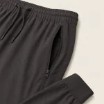Close-up of dark gray joggers showing the waistband, drawstring, zip pocket and cuff
