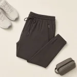 Folded dark gray joggers beside white sneakers and a small zip pouch