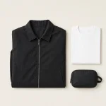 Giacca nera con cerniera piegata accanto a una T-shirt bianca e a un piccolo astuccio nero