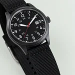 Close-up of a black watch dial with pale numerals, a red hand and a small date window
