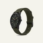 Angled view of a watch with an olive-green woven strap, dark case and tan dial markings