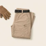 Folded beige cargo trousers with a black belt beside work gloves