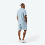 Vista posteriore di un uomo con polo azzurra e shorts coordinati e sneakers bianche