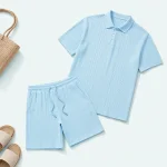 Polo azzurra e shorts stesi accanto a sandali e una borsa intrecciata