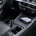 Cargador para coche conectado a una toma de la consola central junto a un teléfono y cables conectados.