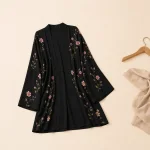 Schwarze, vorne offene Blumen-Abaya flach neben einem Holzbügel und beigefarbenem Stoff ausgelegt
