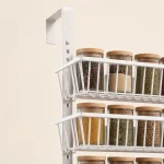Gros plan sur les paniers en fil blanc, les pots à épices et le montant rainuré avec crochet de porte
