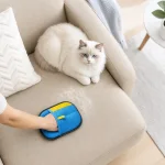 Mão com uma luva azul e amarela num almofadão de sofá, junto de um gato branco